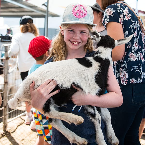 Girl wearing denim cap with peace symbol design carrying a baby goat
